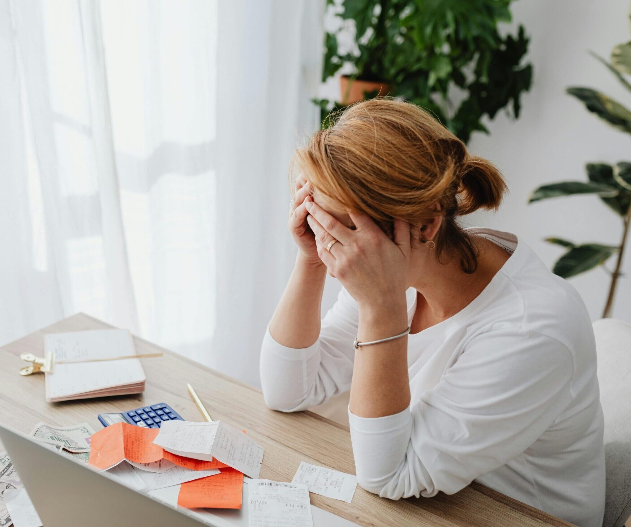 Woman stressed over financial receipts at a desk, dealing with expenses and calculations.