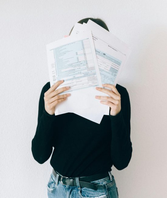 A woman concealing her face with tax forms, illustrating financial stress and paperwork burden.