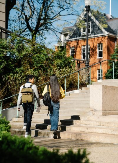 Two young adults walking up outdoor stairs surrounded by greenery and buildings.
